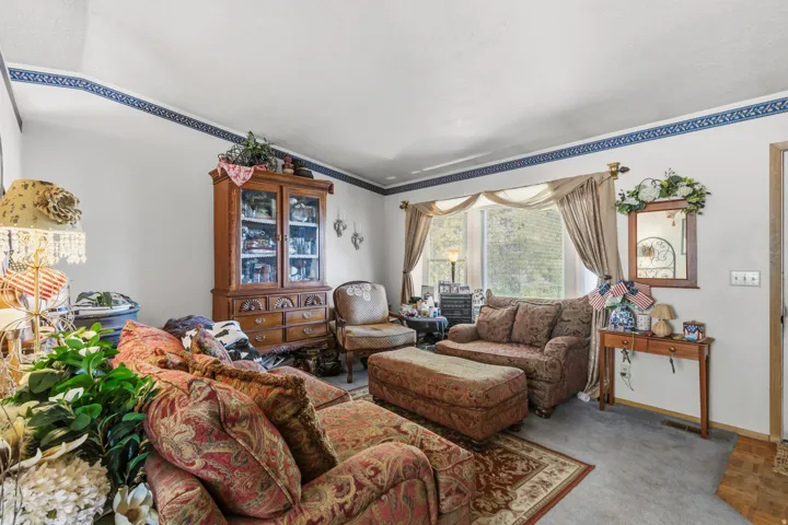 Living area featuring a spacious bay window, patterned carpet, wood-finish flooring, and a decorative border along the ceiling