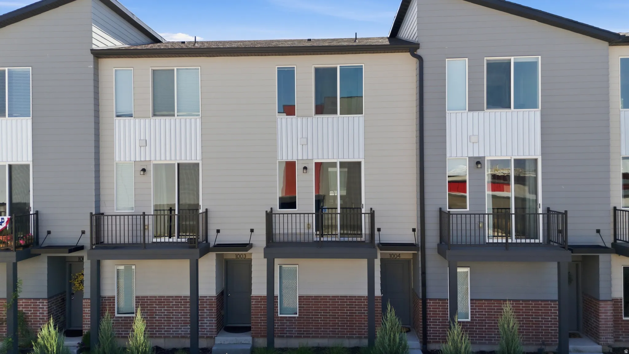 Contemporary townhome facade featuring light gray siding, white vertical paneling, and a brick lower level