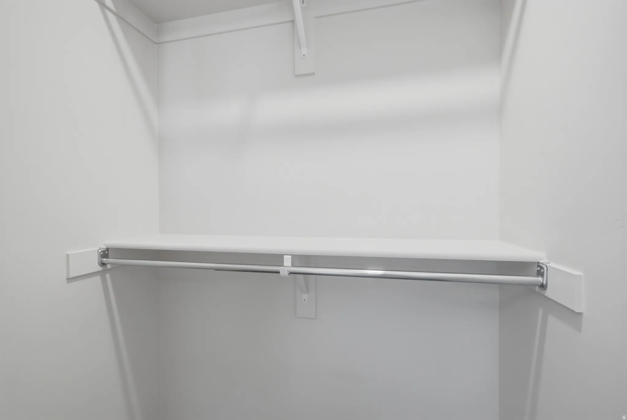 White-painted closet featuring a built-in shelf and chrome hanging rod