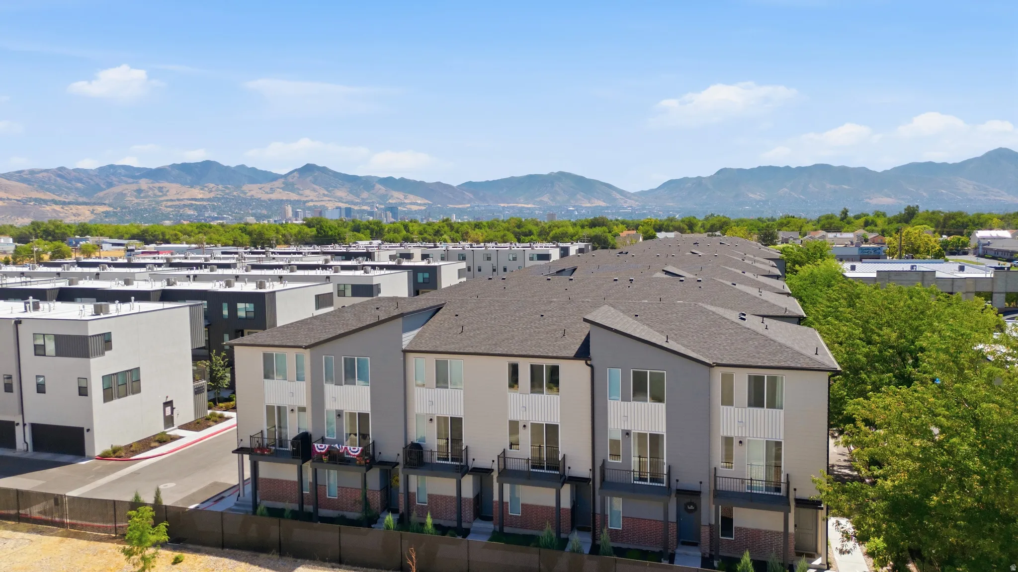 Contemporary multi-story townhome with a dark shingle roof and a mixed material facade including light gray siding, white vertical paneling, and dark brick accents
