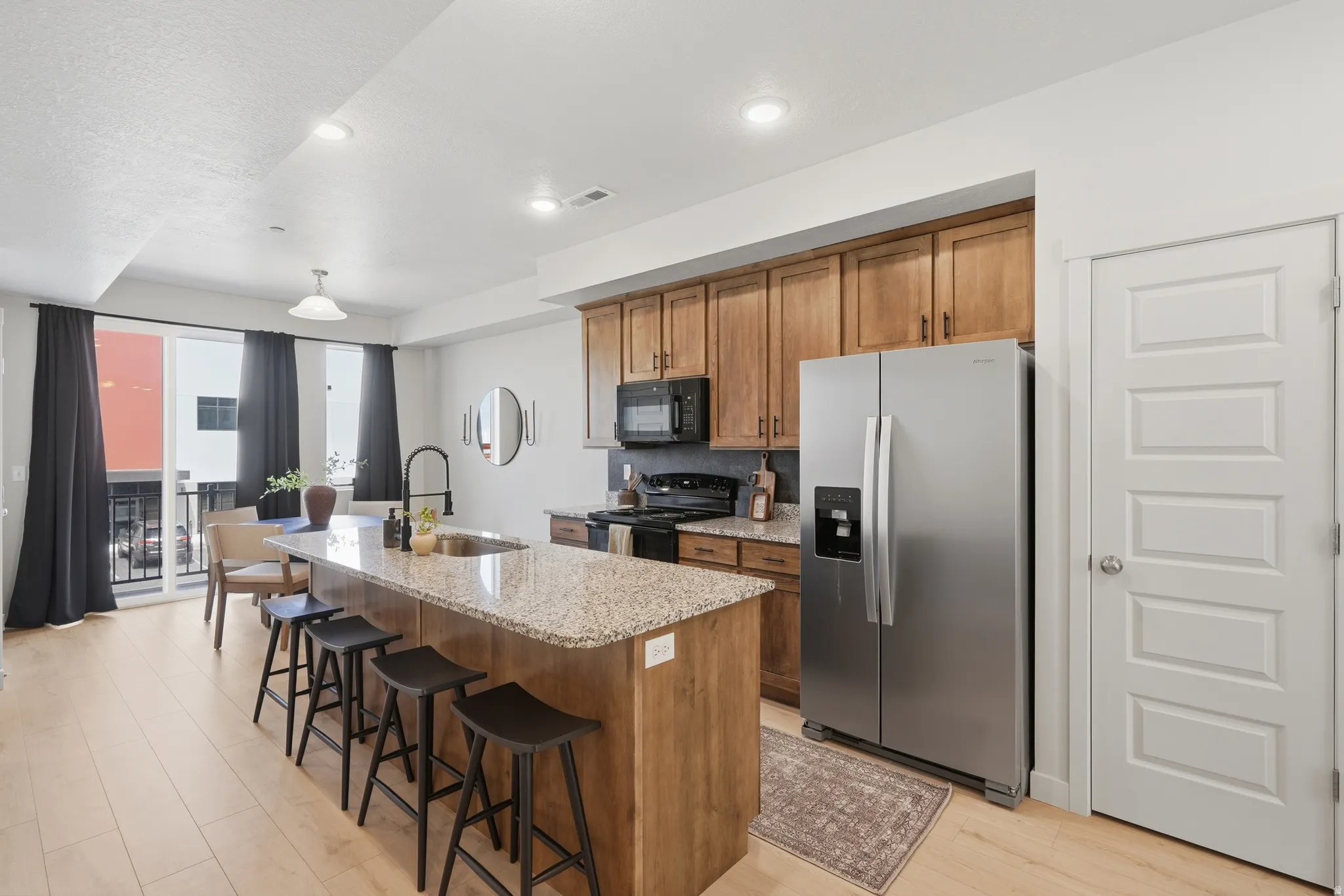 Open-concept kitchen featuring an island with seating, stainless steel appliances, wood cabinetry, and light wood-finish flooring