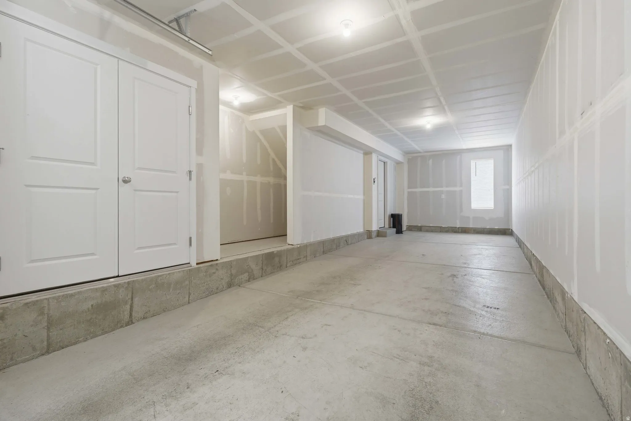 Unfinished interior space featuring a concrete floor, exposed ceiling joists, and drywall-ready walls