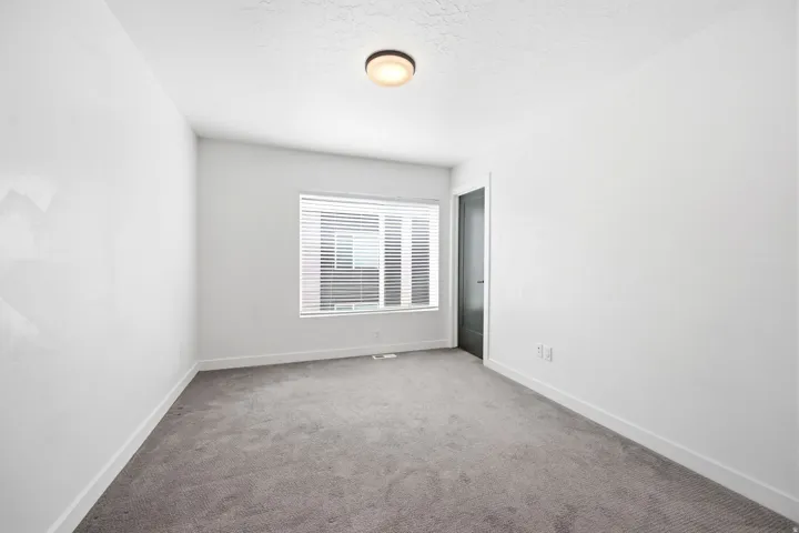 Carpeted interior space featuring a window with blinds, white walls, and a contemporary flush-mount ceiling light