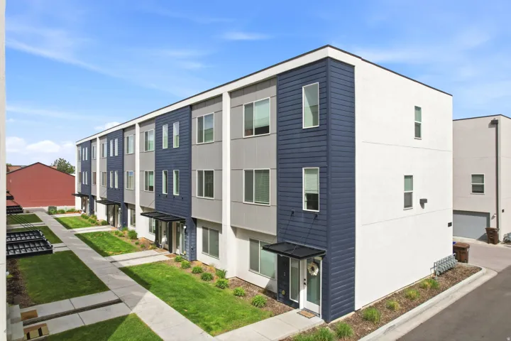 Modern townhome exterior featuring a three-story design, a contrasting facade of white stucco and dark blue siding, and a covered entry