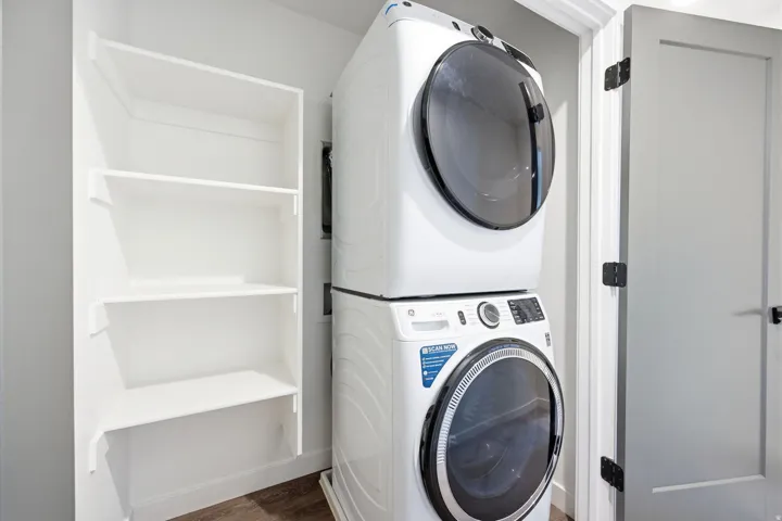 Laundry area featuring a stackable washer and dryer, adjacent built-in shelving, white baseboards, and wood-finish flooring