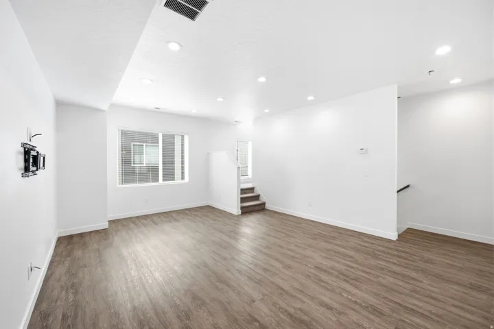 Spacious interior with wood-finish flooring, recessed lighting, white walls, and a window with blinds