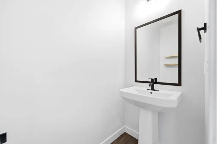 Pedestal sink with matte black faucet, framed mirror, and integrated lighting