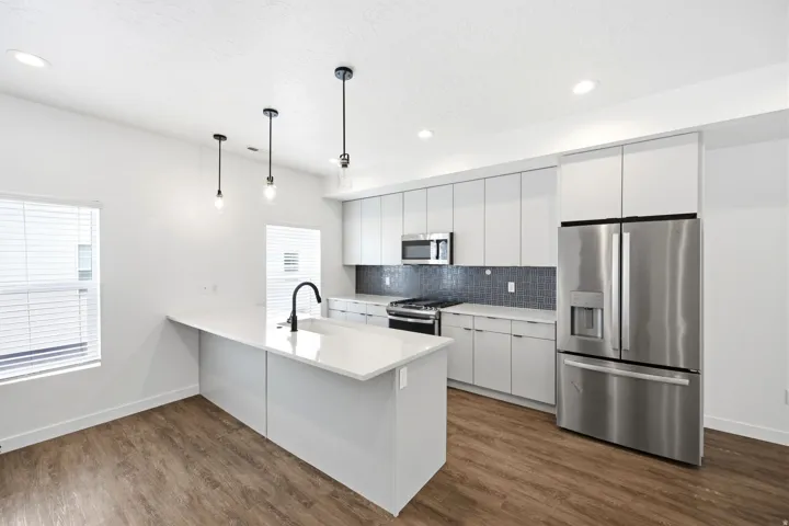 Contemporary kitchen featuring a large island with sink, stainless steel appliances, white flat-panel cabinetry, a dark tile backsplash, and wood-finish flooring