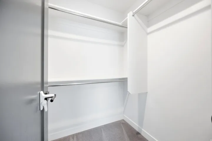 Walk-in closet featuring white walls, gray carpet, and two chrome hanging rods