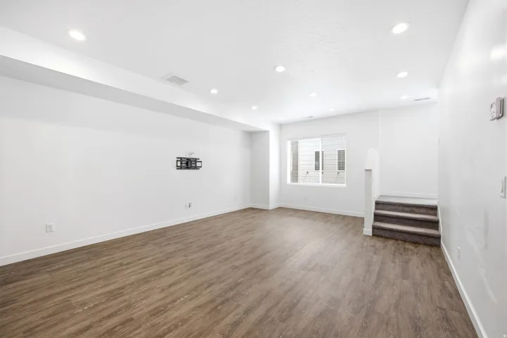 Spacious lower-level room featuring wood-finish flooring, recessed lighting, white baseboards, and a window providing natural illumination