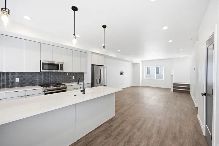 Modern kitchen featuring a large island with white countertops, sleek gray cabinetry, stainless steel appliances, and a dark mosaic tile backsplash