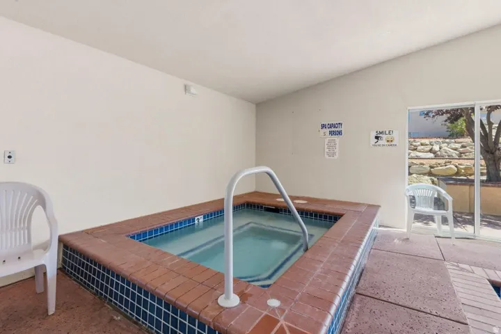 Indoor spa with blue and brown tile surround, white grab rail, and concrete flooring