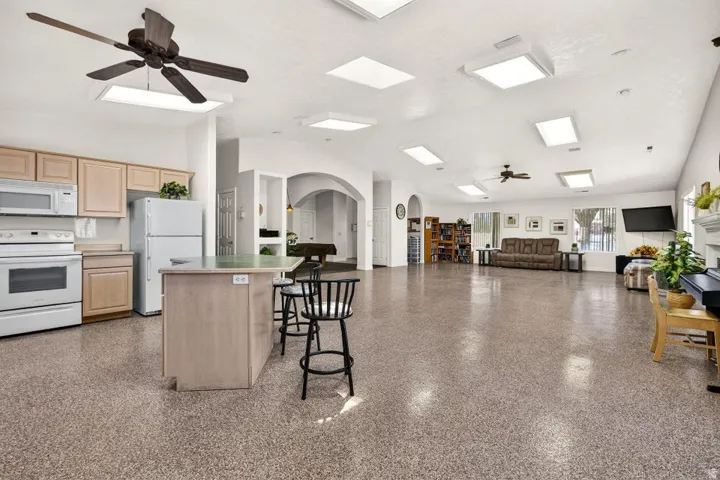 Expansive open-concept room featuring a functional kitchen island, multiple skylights, recessed lighting, ceiling fans, and durable epoxy flooring