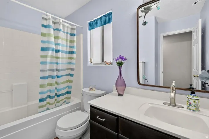 Bathroom with a white tub and shower combination, a dark wood-finish vanity with an integrated white sink, a chrome faucet, and a wall-mounted mirror