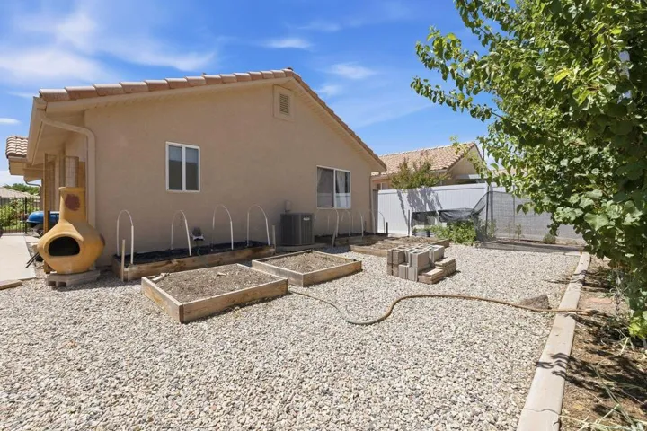 Rear exterior featuring stucco siding, a terracotta tile roof, and multiple raised garden beds