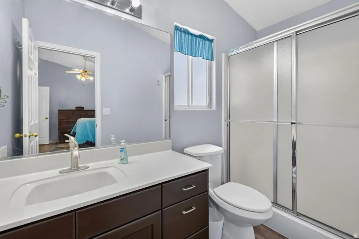 Bathroom featuring a dark wood-finish vanity with a white integrated sink, a large wall-mounted mirror, a toilet, and a shower with frosted sliding doors