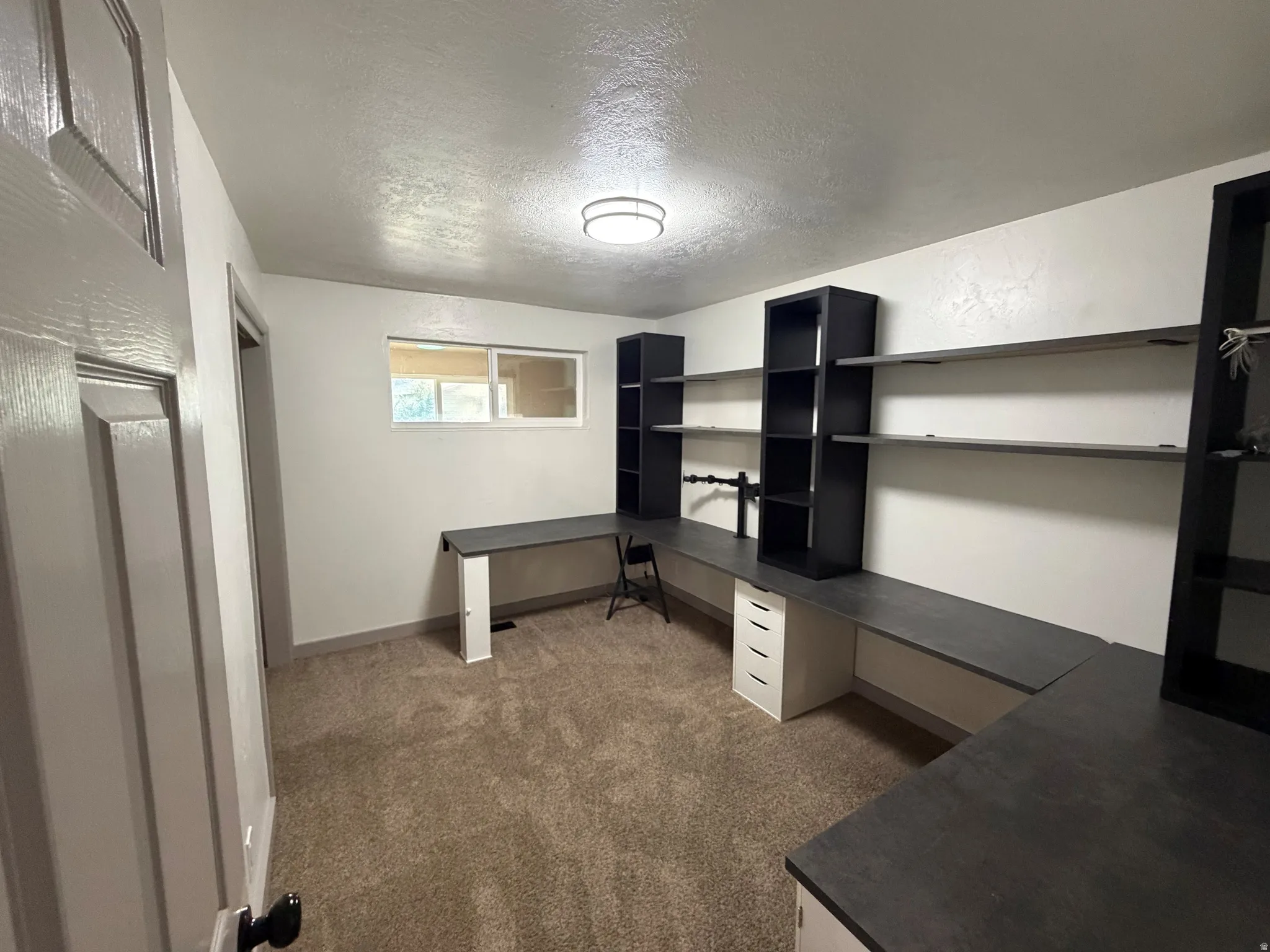Built-in shelving, integrated desk surfaces, wall-mounted display shelves, recessed window, and carpeted flooring
