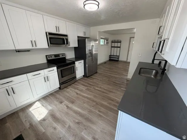 White shaker-style cabinetry, dark countertops, stainless steel appliances, wood-finish flooring, and a modern ceiling light fixture