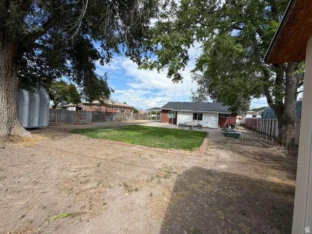 Expansive backyard featuring a partial lawn area, mature trees, and a wooden perimeter fence