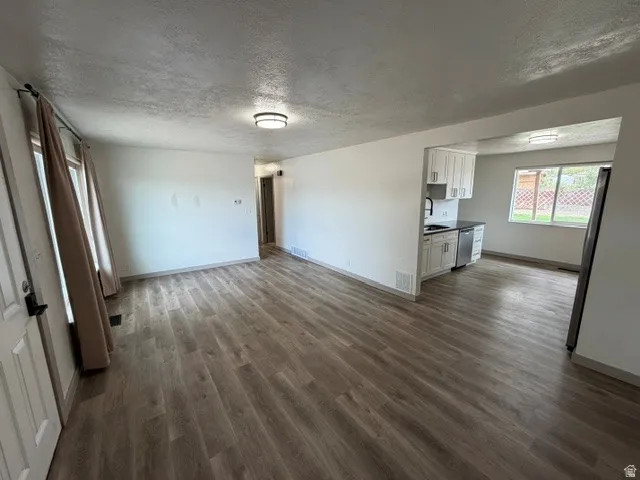 Open-concept living area with wood-finish flooring, recessed lighting, and a kitchen featuring white cabinetry and stainless steel appliances
