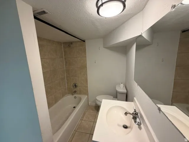 Tile-surround bathtub, ceramic tile flooring, built-in vanity with integrated sink, and overhead flush-mount lighting