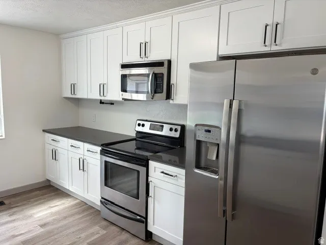 White shaker cabinetry, dark solid surface countertops, stainless steel appliances, wood-finish flooring, and crown molding