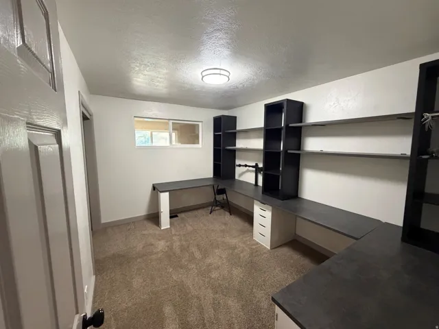 Built-in shelving, integrated desk surfaces, wall-mounted display shelves, recessed window, and carpeted flooring