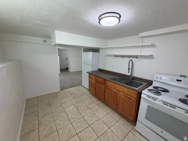Kitchen featuring tile flooring, wood cabinetry, a built-in stainless steel sink, a pull-down faucet, and a ceiling-mounted light fixture