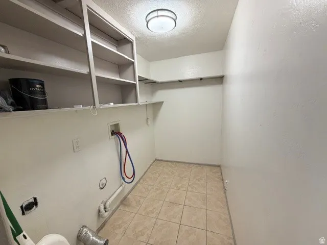 Laundry area featuring a ceiling-mounted light fixture, built-in shelving, tiled flooring, and utility hookups