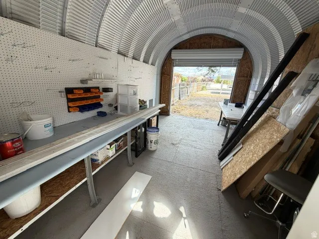 Corrugated metal arched ceiling and walls, concrete flooring, pegboard wall storage, built-in workbench, and roll-up door