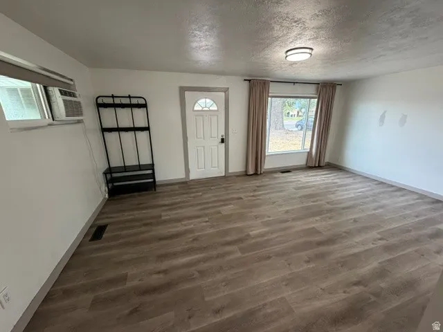 Wood-finish flooring throughout, white walls, and a recessed window with neutral drapes
