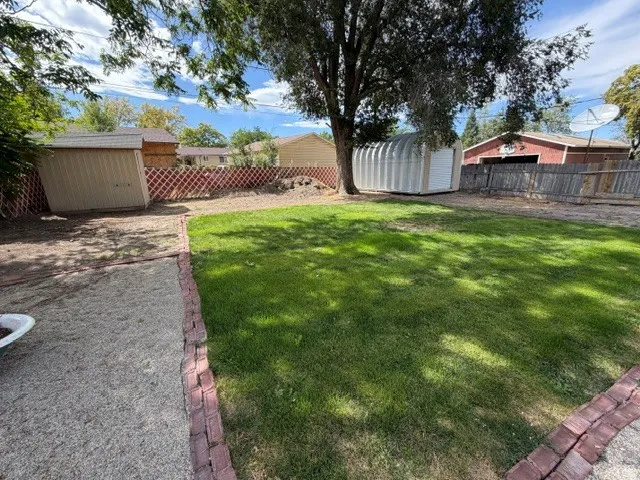 Expansive backyard featuring a lush lawn, a detached storage shed, a metal utility structure, and a red brick border