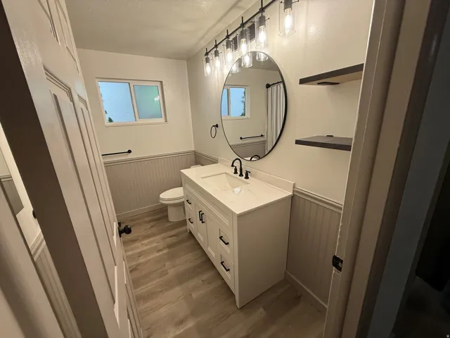 Bathroom featuring a white vanity with integrated sink, a large round mirror, a multi-bulb vanity light fixture, and wood-finish flooring
