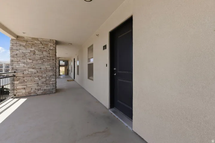 Exterior hallway featuring a stacked stone column, light stucco walls, and a black metal railing