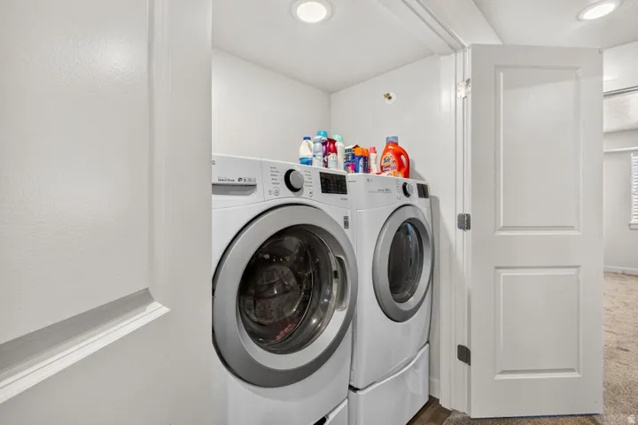 Dedicated laundry area featuring front-loading washer and dryer units with pedestals, recessed ceiling lighting, and a paneled interior door