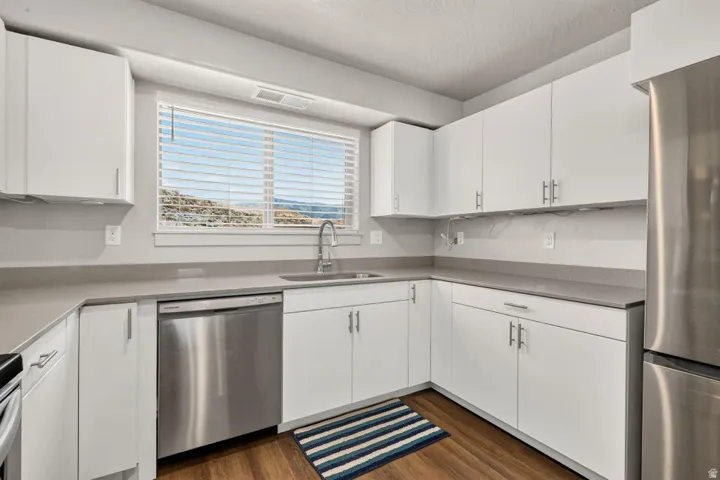 Kitchen featuring white cabinetry, grey countertops, stainless steel appliances, wood-finish flooring, and a large window with horizontal blinds