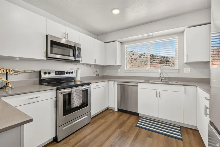 Modern kitchen featuring white cabinetry, stainless steel appliances, wood-finish flooring, and light-toned countertops