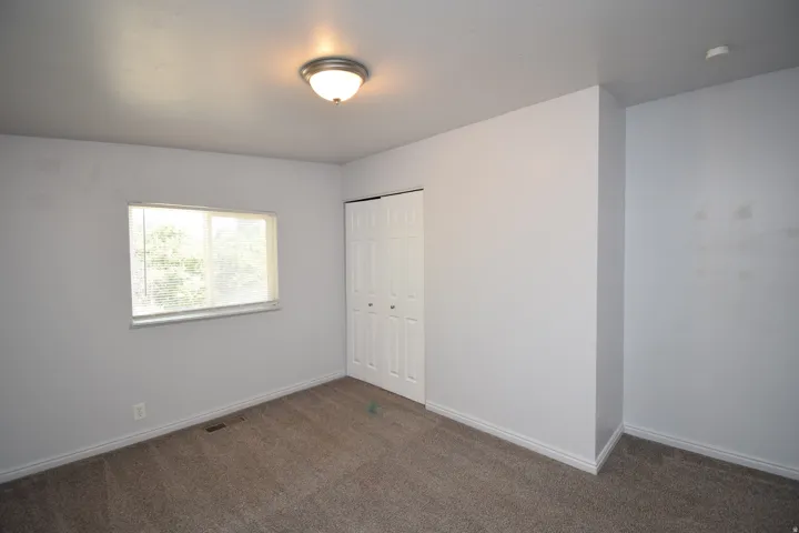 Carpeted room featuring a window with blinds, white trim, bi-fold closet doors, and a ceiling-mounted light fixture