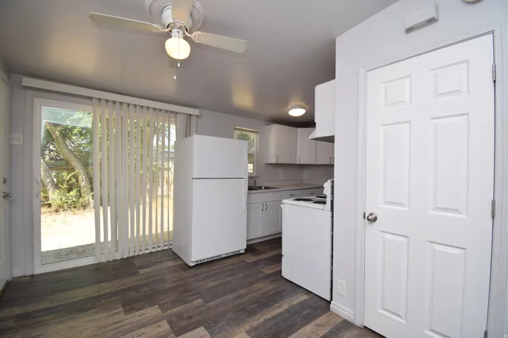 Kitchen featuring white cabinetry and appliances, wood-finish flooring, and a sliding glass door to the exterior