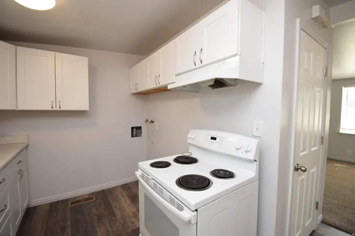 Kitchen area featuring white cabinetry, a white electric range with range hood, wood-finish flooring, and white countertops