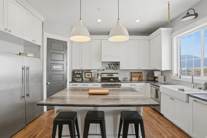 Spacious kitchen featuring an expansive center island, white shaker cabinetry, stainless steel appliances, a farmhouse sink, and wood-finish flooring
