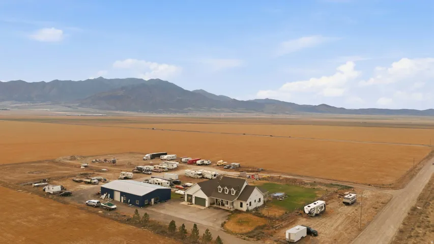 Rural property featuring a single-family residence, a large blue outbuilding, a smaller white outbuilding, and expansive surrounding land