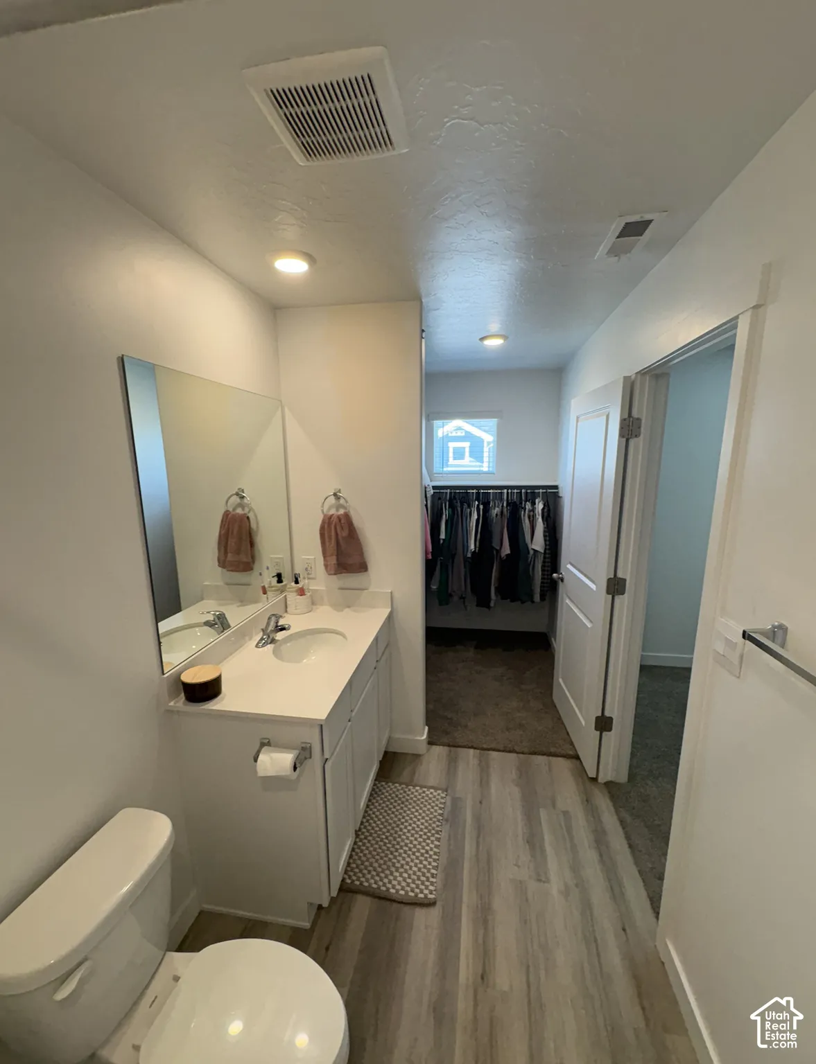 Bathroom featuring a single vanity with a white countertop and undermount sink, a white toilet, and wood-finish flooring