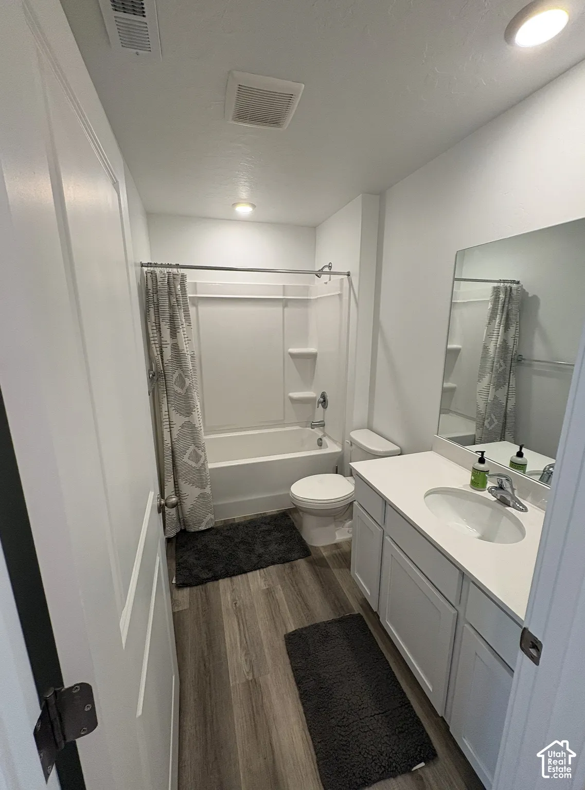 Full bathroom featuring a white tub/shower combination, wood-finish flooring, white vanity with an integrated sink, and an overhead recessed light