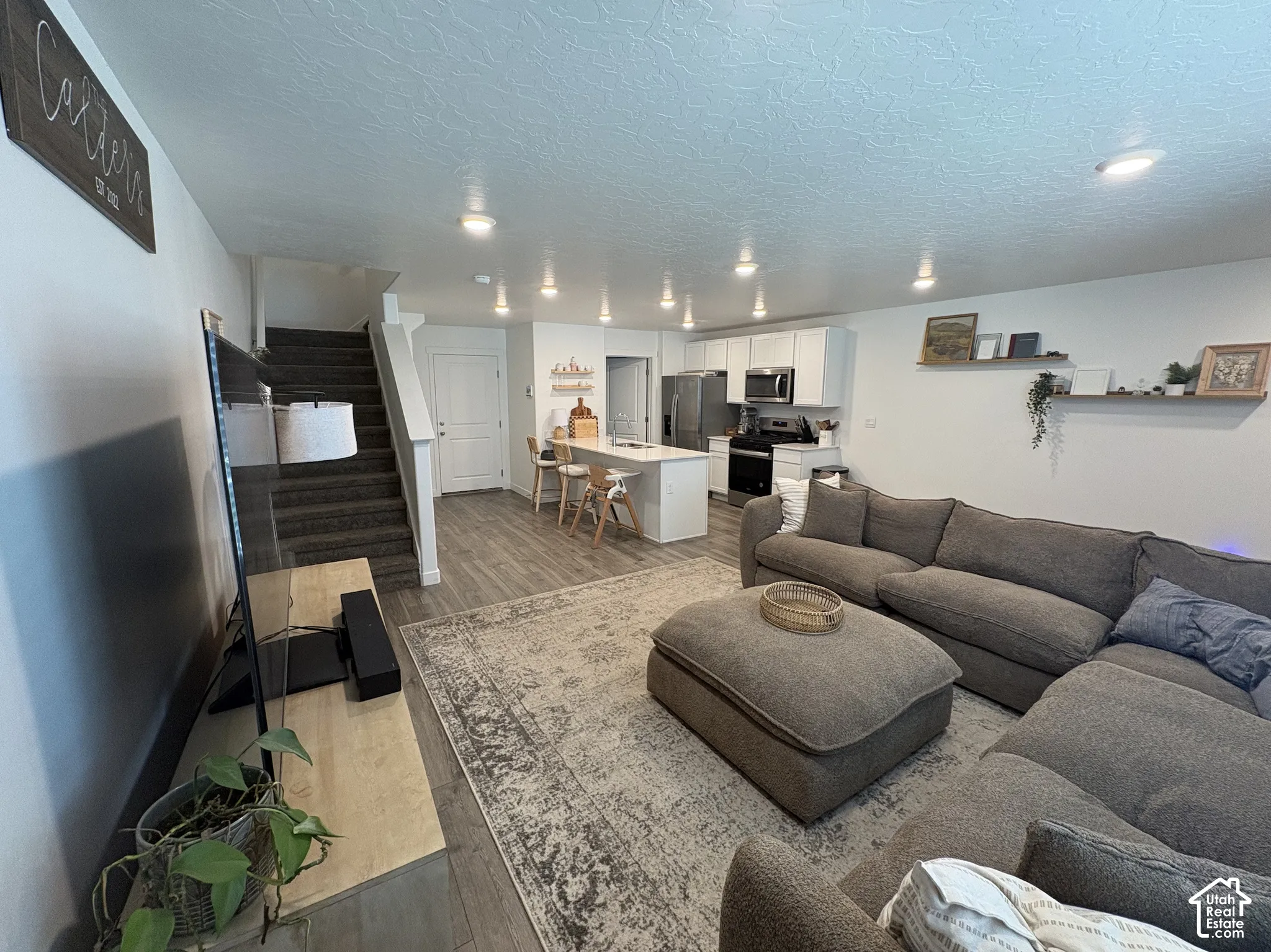 Open-concept living area featuring wood-finish flooring, recessed lighting, white walls, and a staircase with carpeted treads