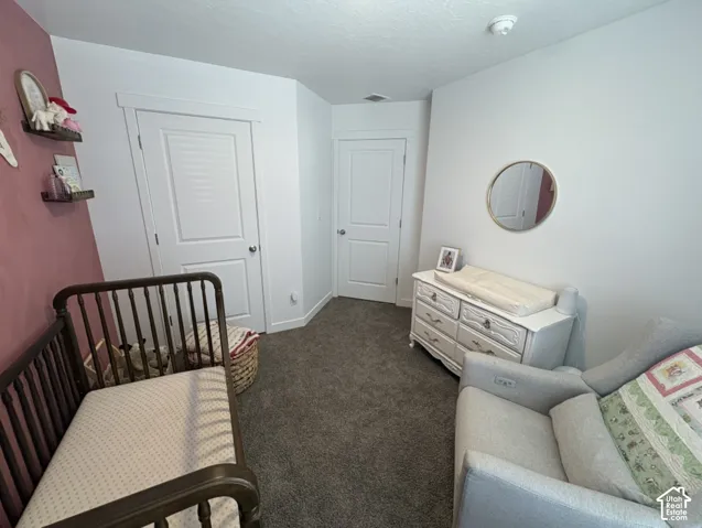 Carpeted interior space featuring white walls with one accent wall, two white louvered doors, and a ceiling-mounted smoke detector