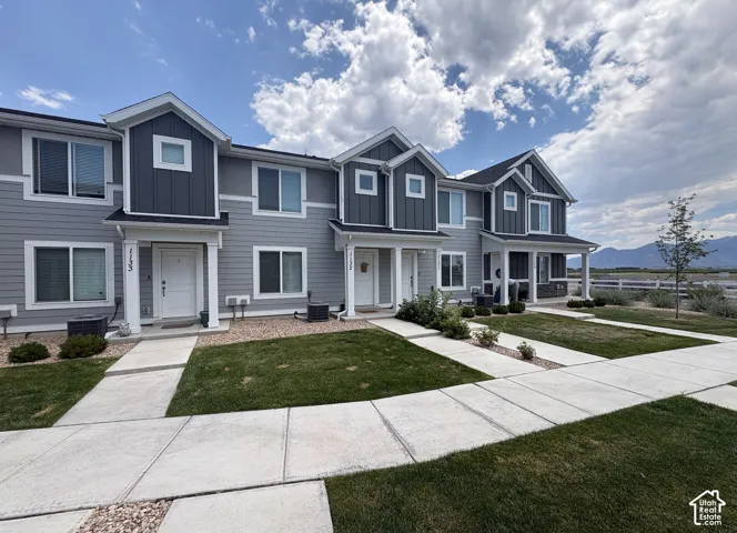 Modern townhome exterior featuring gray siding, white trim accents, multiple windows, and a covered entry