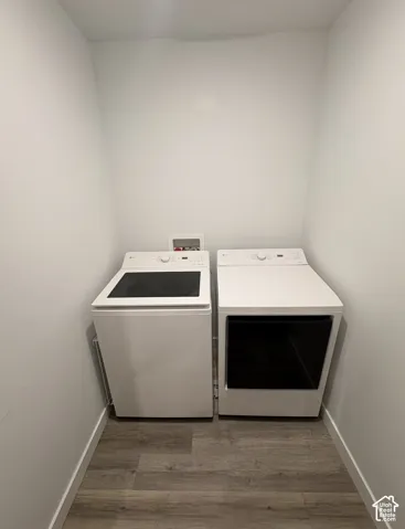 Dedicated laundry area featuring white appliances, wood-finish flooring, and white baseboards