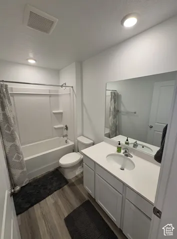 Bathroom featuring wood-finish flooring, a white vanity with integrated sink, a large wall-mounted mirror, a standard toilet, and a bathtub with a shower surround