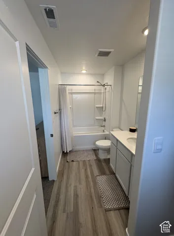 Full bathroom featuring a white tub/shower combination, a vanity with a white countertop and double-door cabinetry, a toilet, and wood-finish flooring